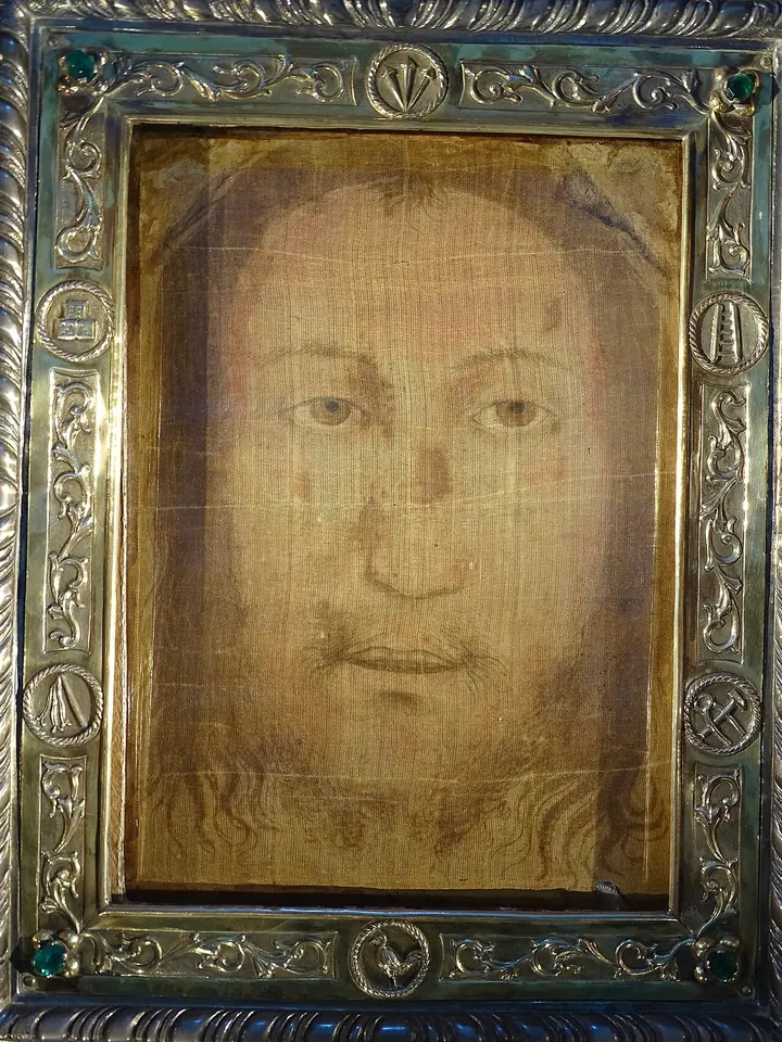 Close photograph of a thin, translucent cloth showing a bearded face with open eyes, set in an ornate silver frame