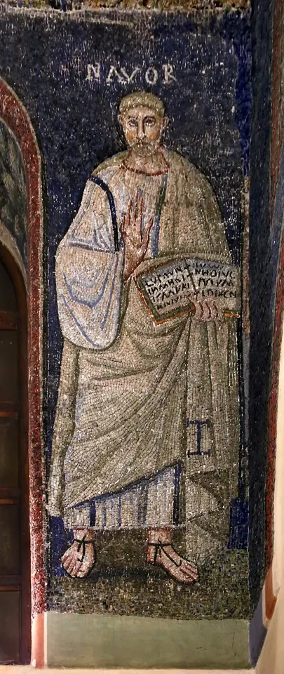 A standing mosaic figure of the martyr St. Nabor in a white robe holding an open book, against a blue background