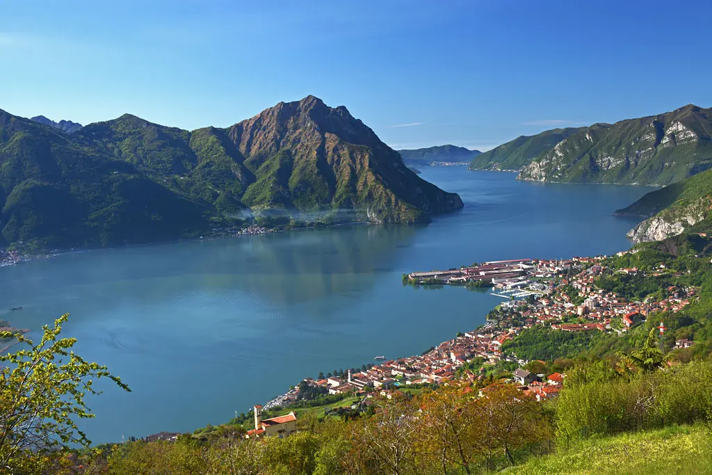 View from a green hillside over a long blue lake between steep mountains, with the town of Lovere spread along the near shore