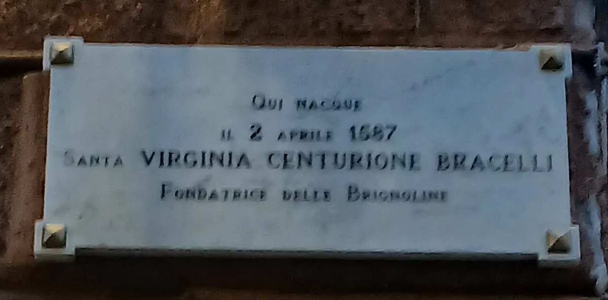 A white marble plaque with brass corner studs reading Qui nacque il 2 aprile 1587 Santa Virginia Centurione Bracelli fondatrice delle Brignoline