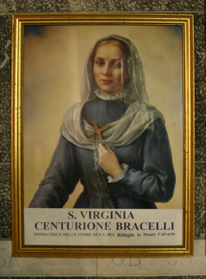 A framed painting of a young woman in a blue-gray dress and sheer white veil holding a wooden crucifix to her heart, above a label reading S. Virginia Centurione Bracelli