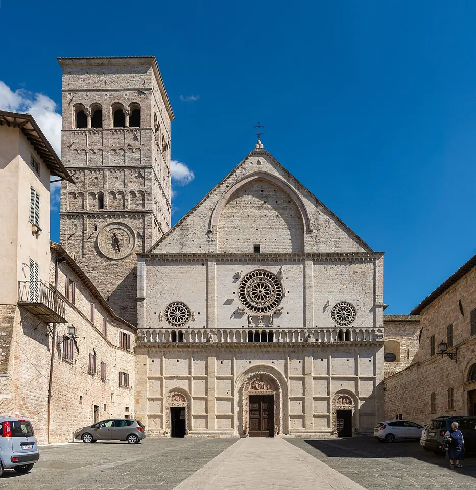 The pink-and-white Romanesque stone facade of Assisi's cathedral with three rose windows and carved portals