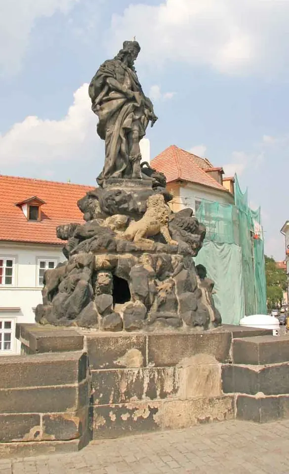 Baroque stone statue of St. Vitus standing on top of a rocky outcrop on Charles Bridge, with carved lions around a cave below him