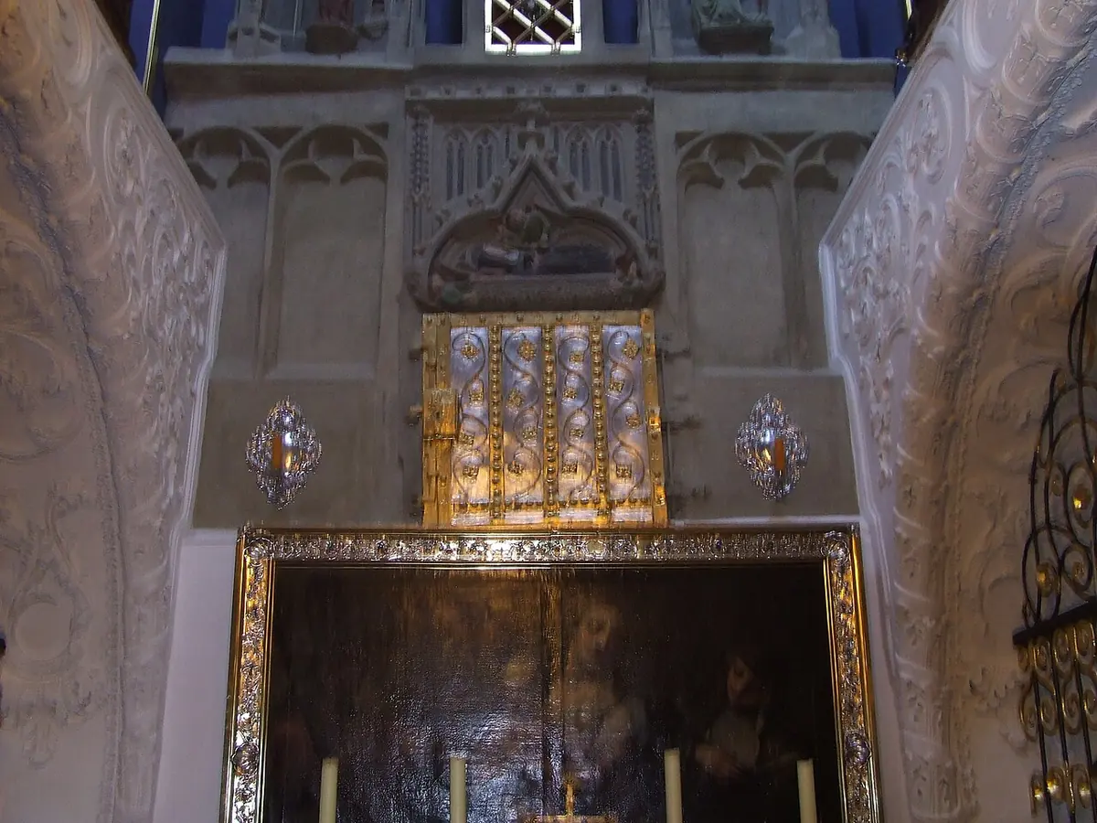 A small vaulted crypt chapel with white stucco walls, a carved stone shrine and a golden reliquary panel above an altar lit by candles
