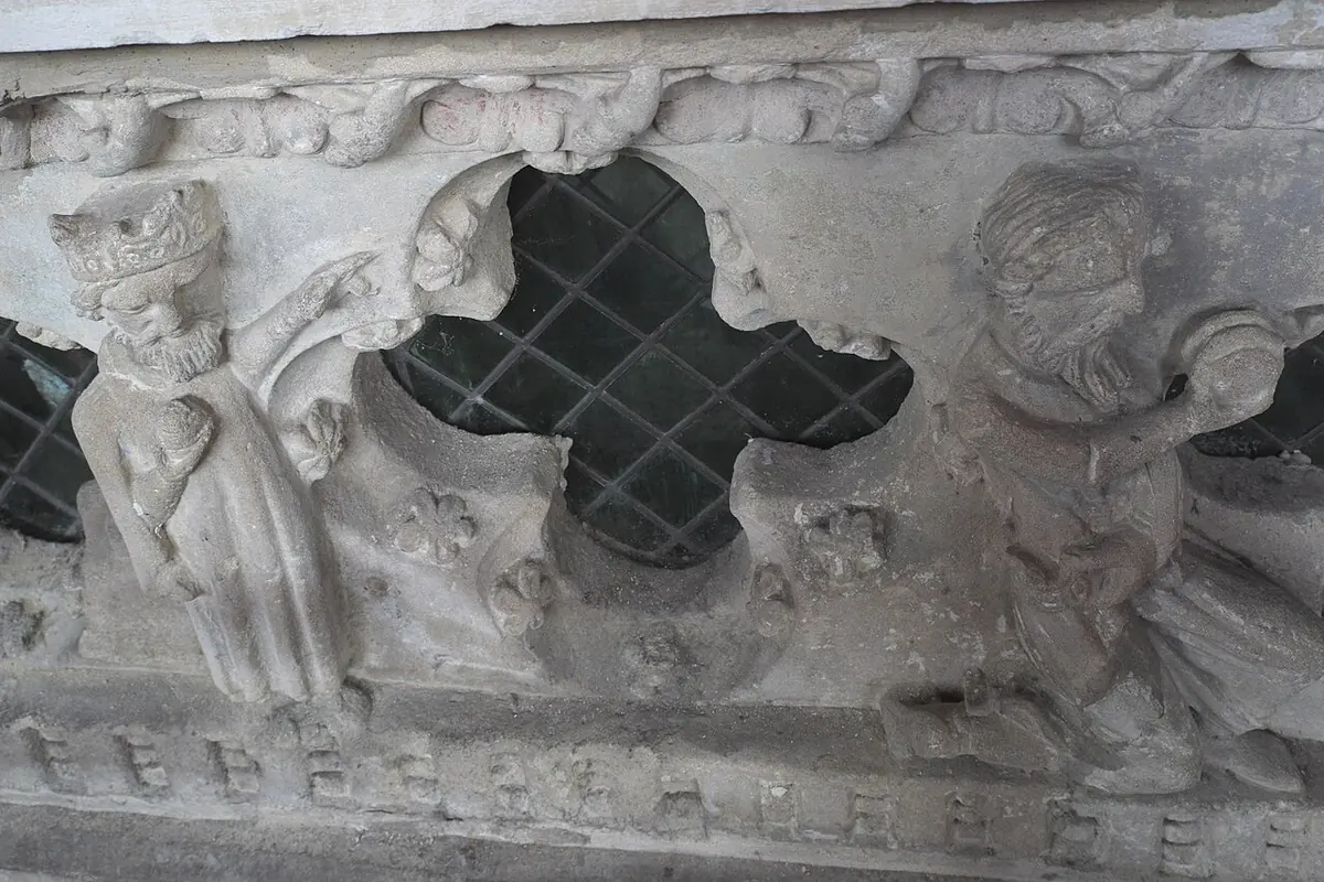 A carved stone beast with an open mouth crouching beneath the feet of a recumbent effigy