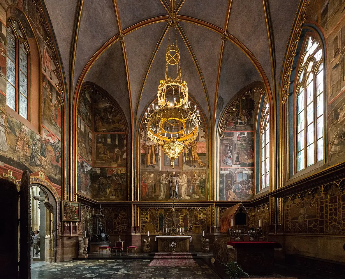 A Gothic chapel with a ribbed vault, walls covered in wall paintings and set with polished semiprecious stones, and a gilded chandelier above the altar