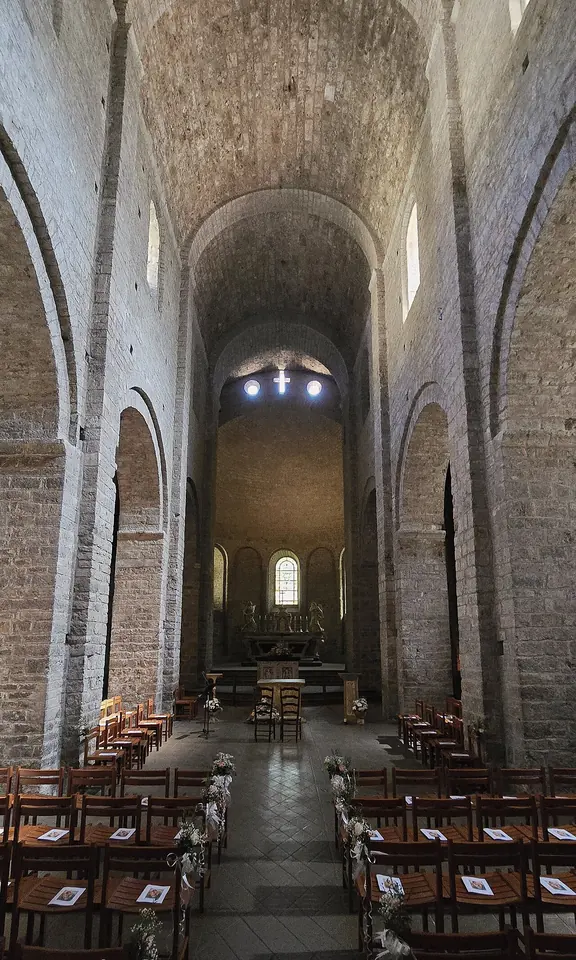 The tall, narrow barrel-vaulted nave of a Romanesque abbey church, looking down rows of chairs toward a lit apse