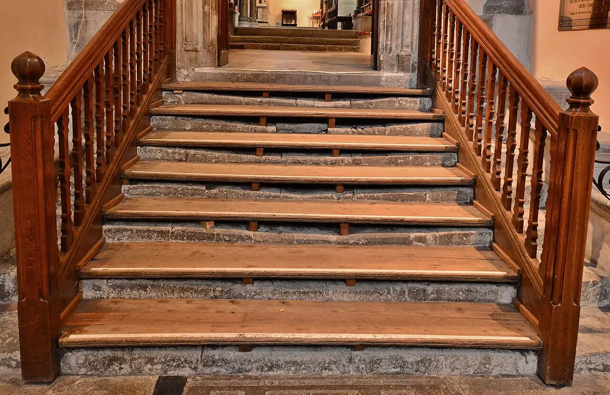 A flight of old stone steps, deeply hollowed by wear and now covered with wooden treads, between wooden handrails