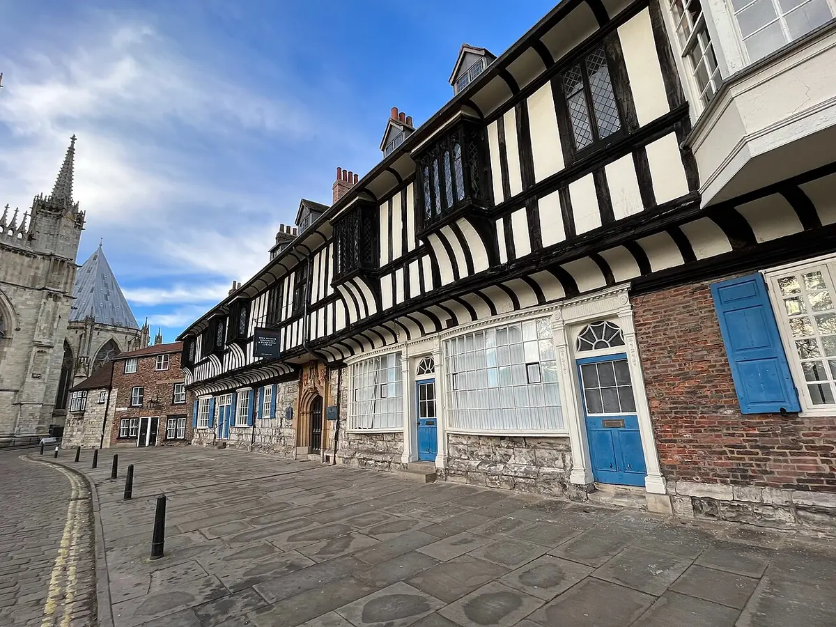 A long black-and-white timber-framed medieval building on a cobbled street, with the tower of York Minster rising behind it