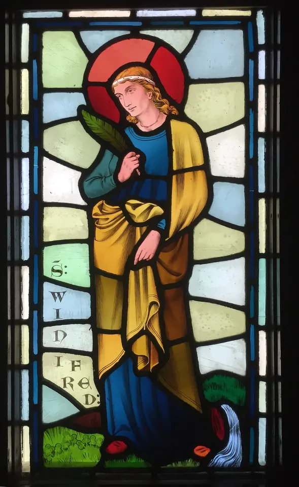 Stained-glass panel of a young saint with a red halo in a blue robe and gold cloak, holding a palm, with her name beside her and a small stream of water at her feet