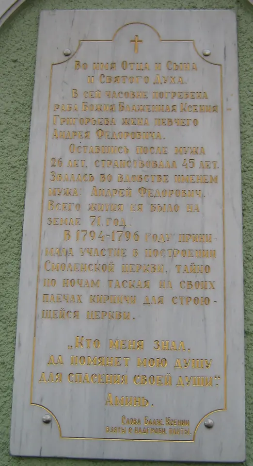 A white marble plaque with a cross and gilded Russian text set into the green wall of the chapel