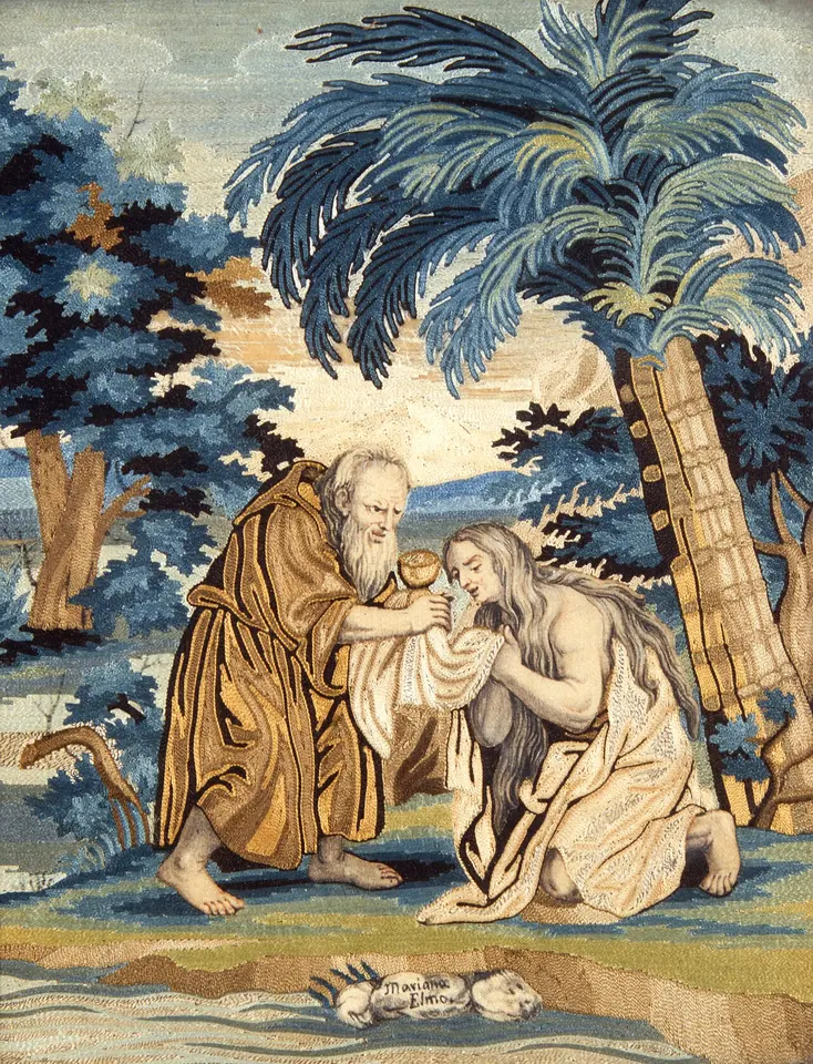Embroidered picture of an old bearded monk in a brown habit kneeling to give Communion from a chalice to a kneeling woman with long hair, under blue palm trees