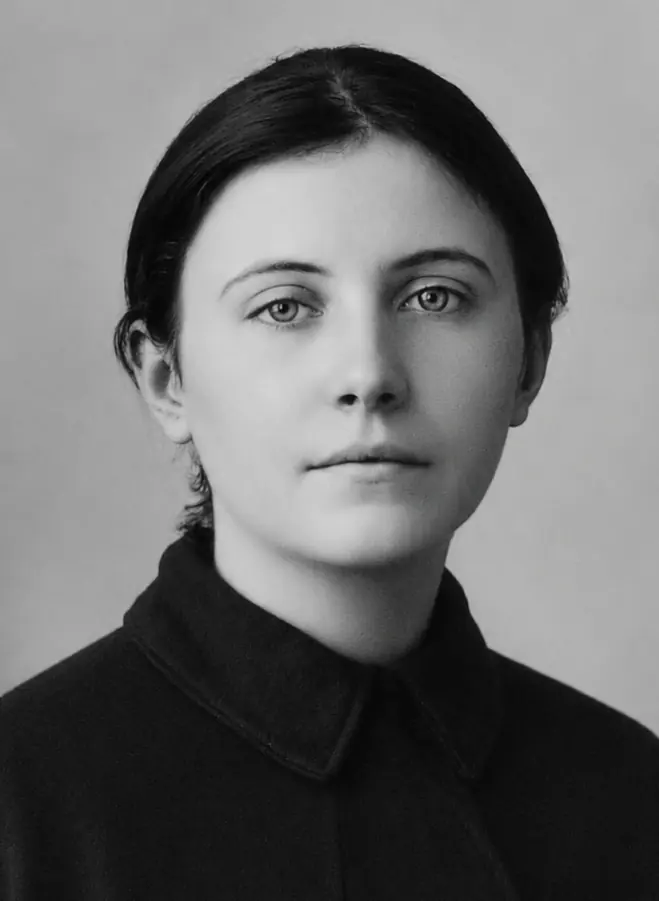 Black and white photograph of a young woman with dark hair pulled back, wearing a plain dark dress with a high collar