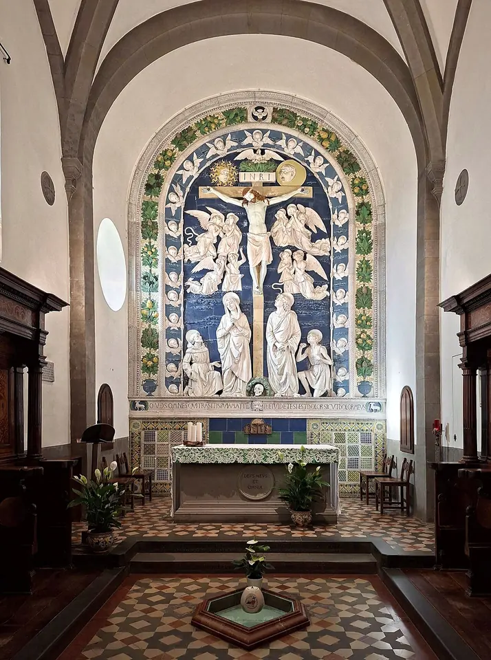 A vaulted chapel with a large blue and white glazed terracotta Crucifixion above the altar, framed by a garland of fruit, with a patterned floor