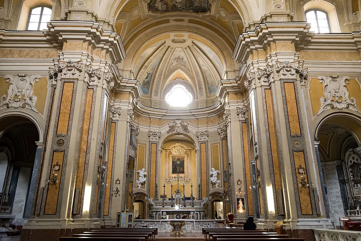 Bright Baroque church interior in cream and gold, with marble pilasters, a dome above and a high altar framed by columns