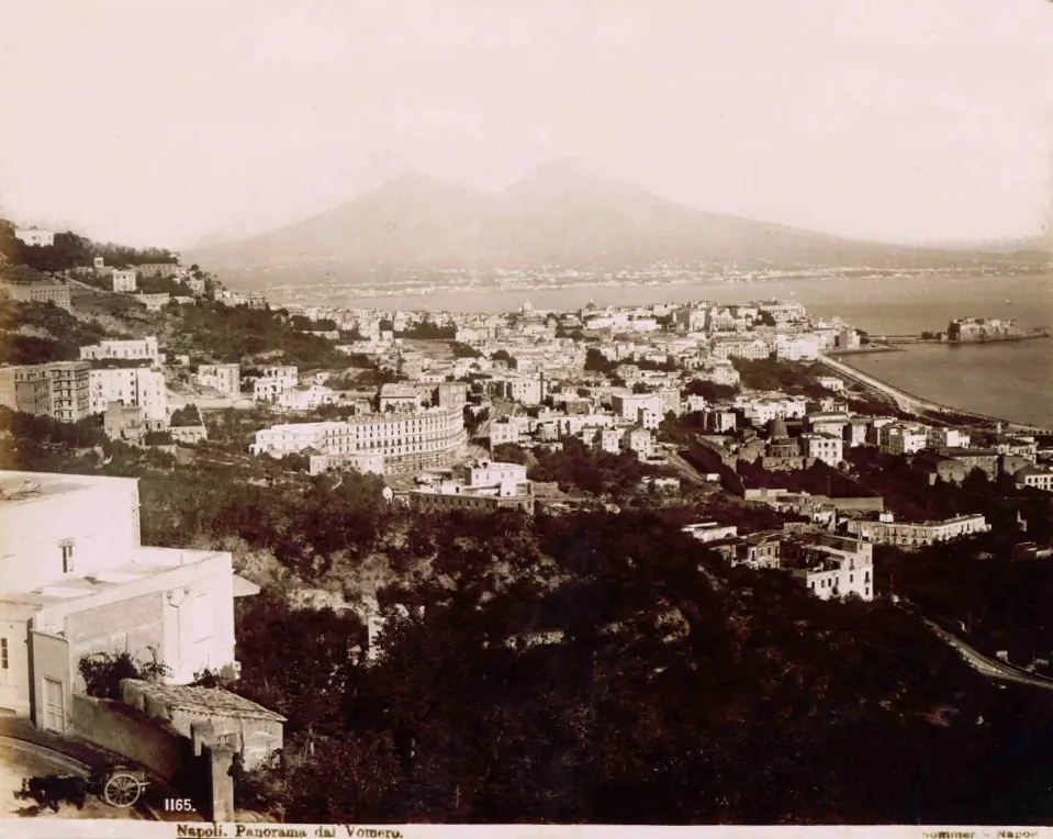 Old sepia photograph of Naples seen from the Vomero hill, with rooftops sloping down to the bay and Mount Vesuvius in the distance