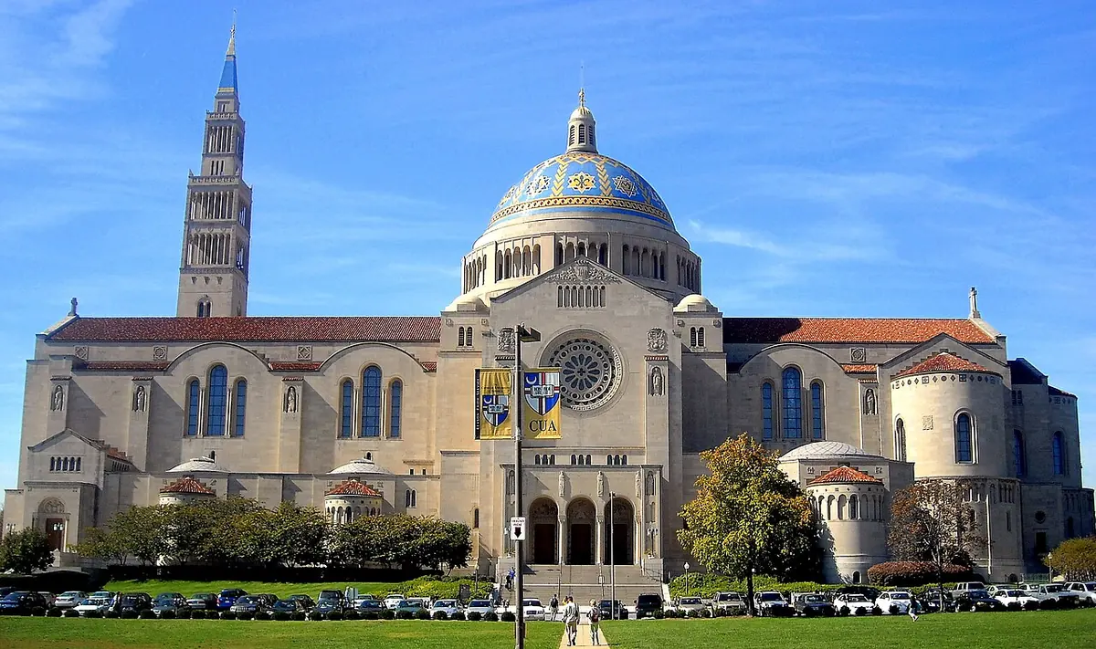A huge pale stone church with a blue and gold tiled dome and a tall bell tower, seen across a lawn