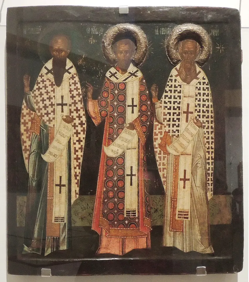 Russian icon of three bishops in white and red vestments with crosses, the middle one in a red patterned robe, each holding a scroll, under silver halos