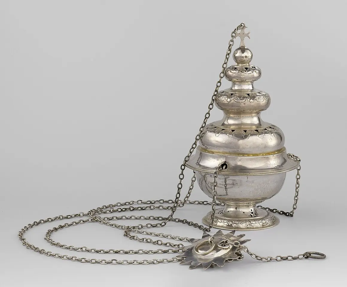 An 18th-century silver thurible from Haarlem with a domed, pierced lid and leaf decoration, its long chains spread out on the table