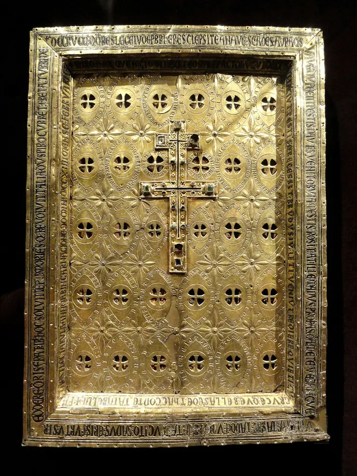 A gilded silver panel pierced with rows of small round openings, with a small double-armed cross set in the center and an inscription around the frame