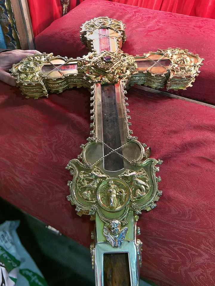 A large gilded silver cross-shaped reliquary with dark wood visible behind glass along its arms, resting on red damask