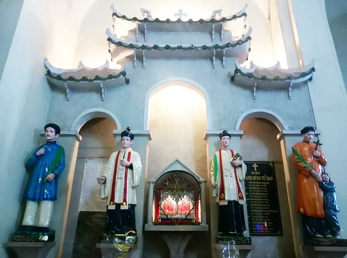 Chapel with a pagoda-style roofline and four painted statues of martyrs in Vietnamese dress and priestly vestments around a small shrine with red candles