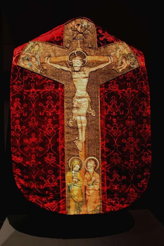 Back of a medieval red velvet chasuble with a woven pattern and a gold embroidered cross showing the Crucifixion