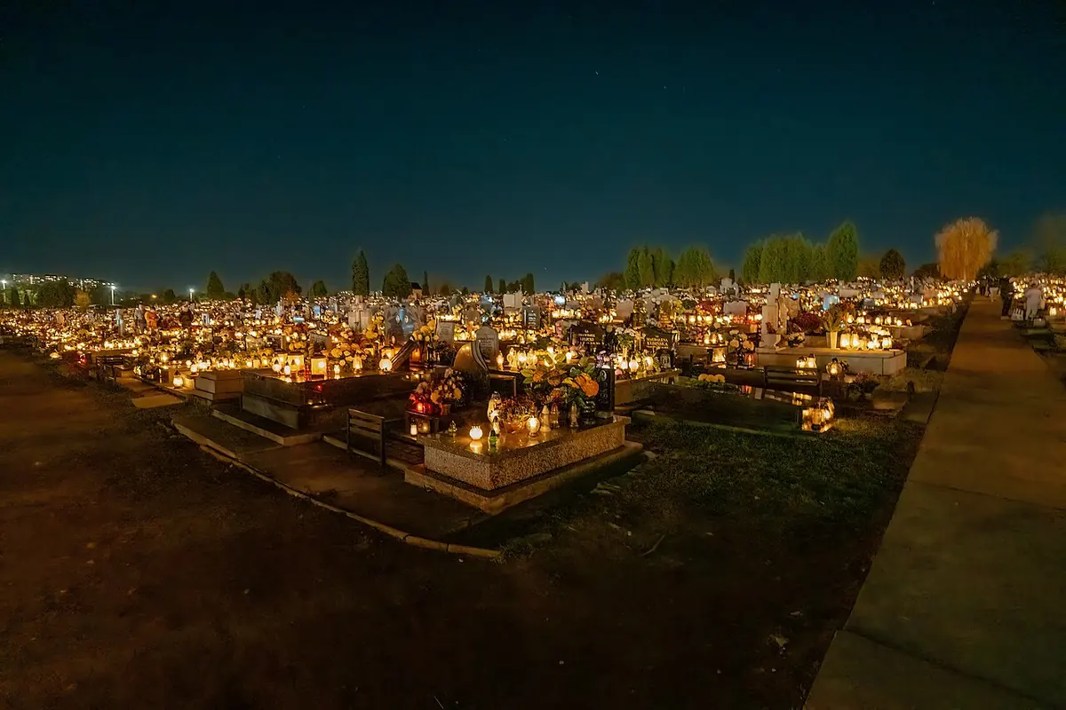 A wide cemetery at night glowing with thousands of red and white grave candles under a dark blue sky
