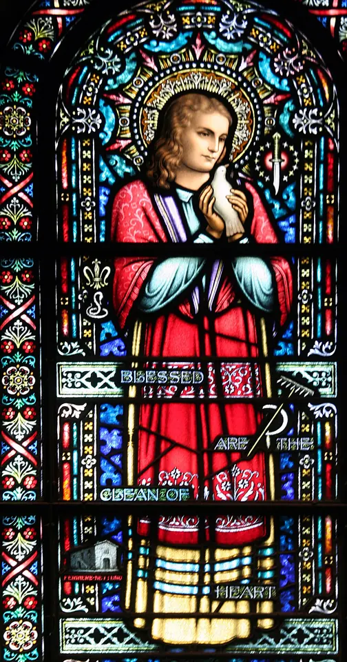 Stained-glass window of St. Maria Goretti in a red dress with a halo, hands joined in prayer, with lilies and a palm in the borders